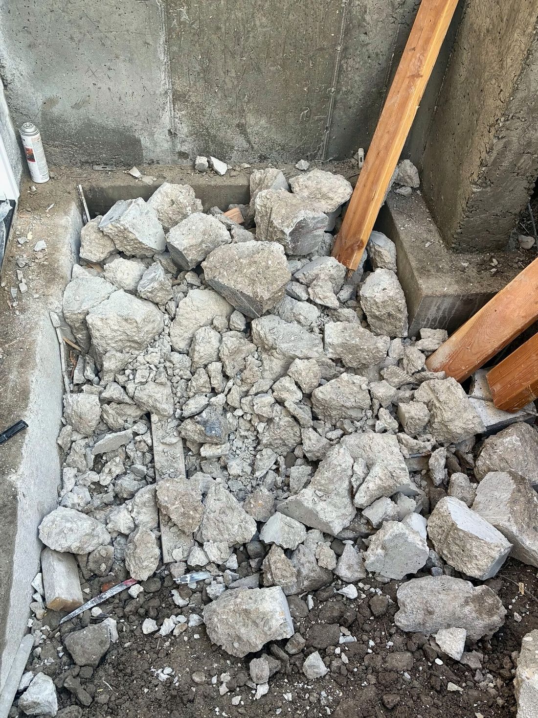 Broken concrete removed during demolition beside a foundation wall