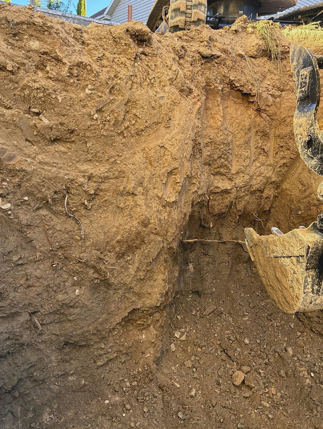 Compact excavator cutting a deep excavation beside a Utah home