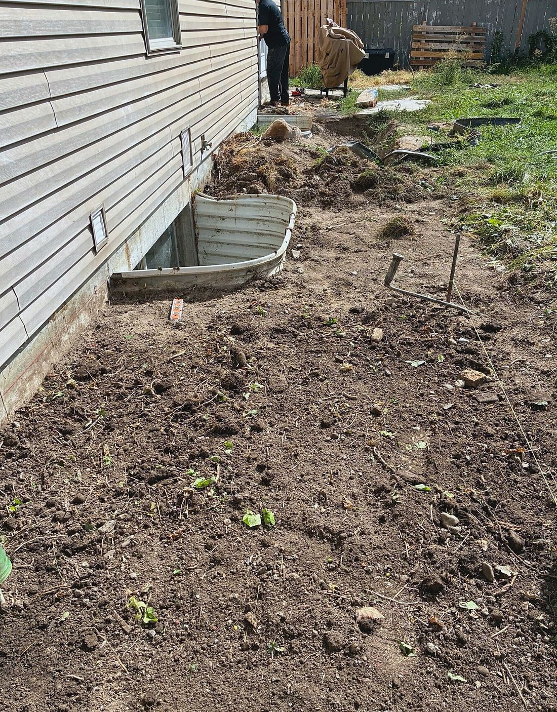 Side yard and existing window well before excavation for a concrete walkout stairwell